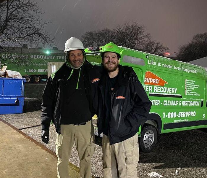 Two employees standing in front of a green van while it's snowing.